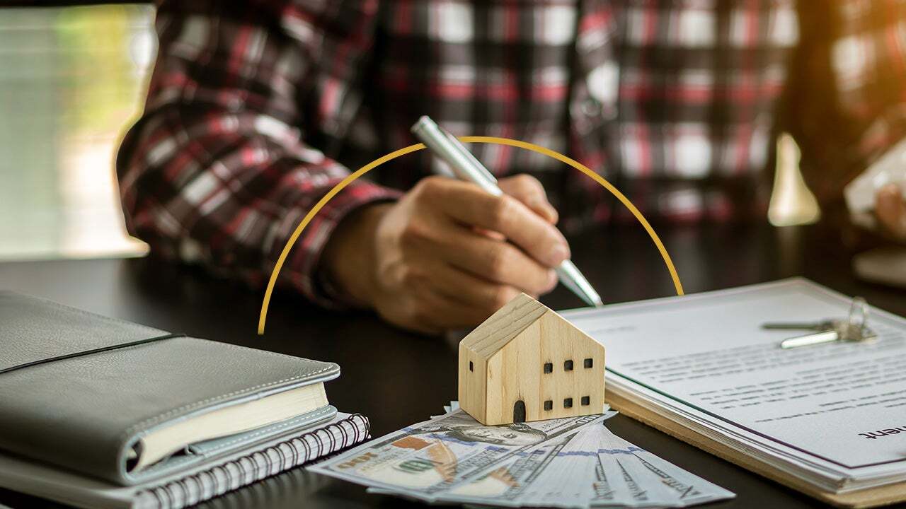 Home figure with papers on a desk, hand with pen in background.